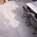Houten eettafel en rieten stoelen op grote lichtgrijze GeoCeramica 60x60 tegels