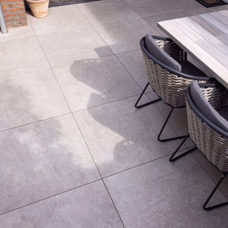 Houten eettafel en rieten stoelen op grote lichtgrijze GeoCeramica 60x60 tegels