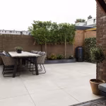 Achtertuin met eettafel, olijfboom en bakstenen muur op GeoCeramica Palanta Plus Gold tegels