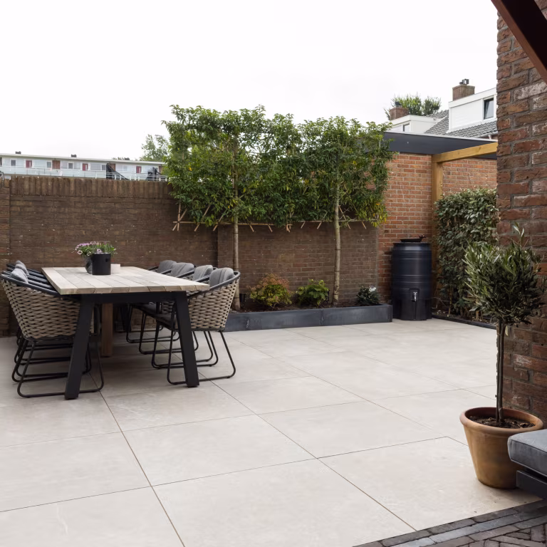 Achtertuin met eettafel, olijfboom en bakstenen muur op GeoCeramica Palanta Plus Gold tegels