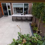 Terras achter woning met eettafel en haag op GeoCeramica 60x60 Palanta Plus Gold tegels