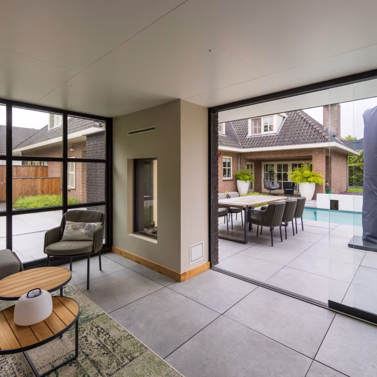 Veranda met zithoek en open glazen wand, eettafel op terras en zwembad op achtergrond