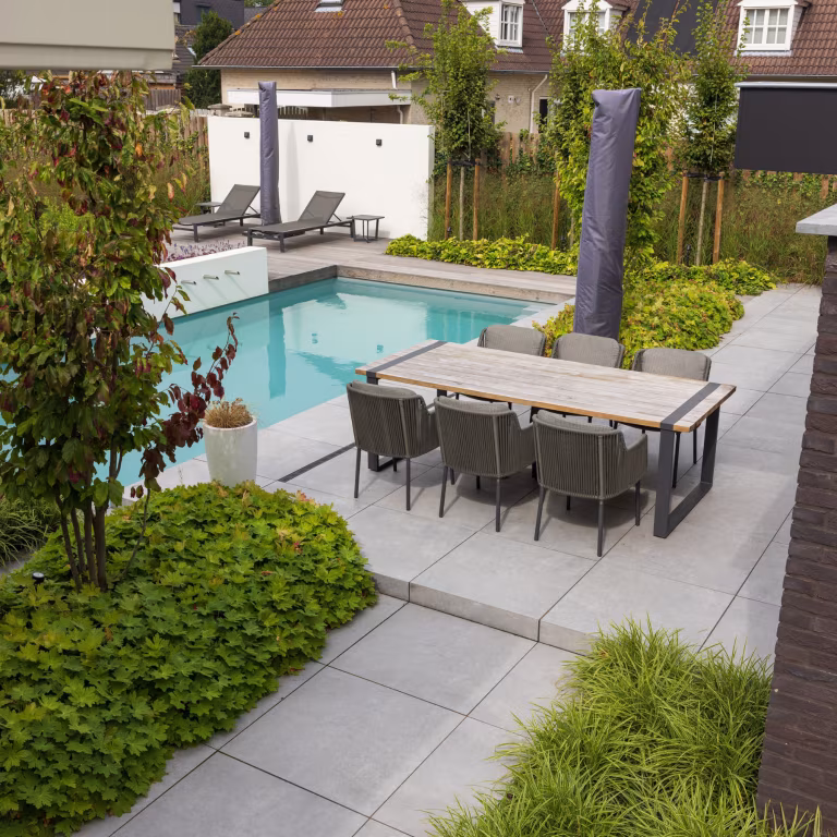 Tuin met zwembad, lichtgrijze keramische terrastegels, eettafel en ligbedden op de achtergrond
