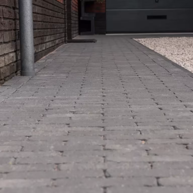 Oprit van antraciet Tambour waalformaat klinkers langs gevel en grindstrook