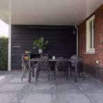 Overdekt terras met zwarte houten wand, eettafel en Tambour Antraciet waalformaat tussen tegels