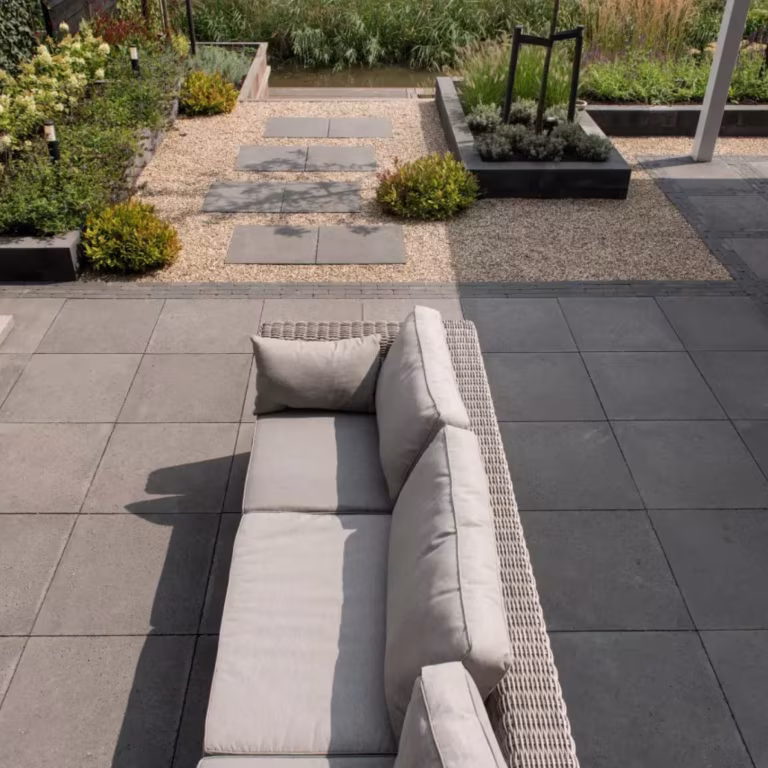 Terras met grijze tegels, rotan loungebank en grindtuin met Tambour Antraciet waalformaat
