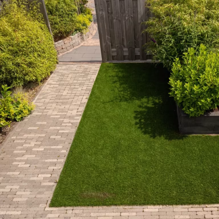 Klinkerpad langs kunstgrasstrook met houten poort, struiken en plantenbak