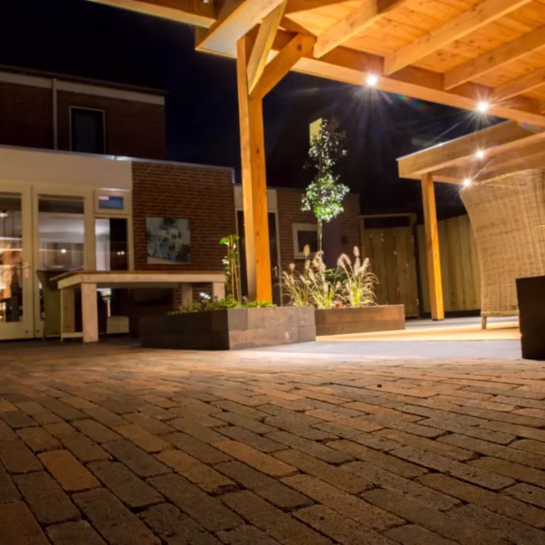Avondfoto van verlicht overdekt terras met Tambour Brons waalformaat in verband
