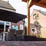 Terras onder houten overkapping met parasol, tuinstoelen en Tambour Brons waalformaat