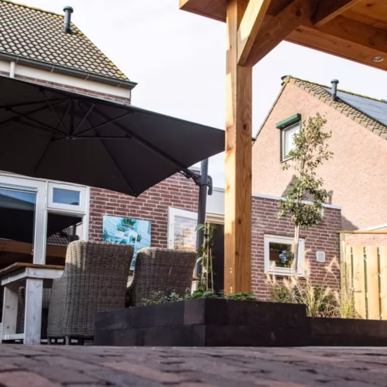 Terras onder houten overkapping met parasol, tuinstoelen en Tambour Brons waalformaat