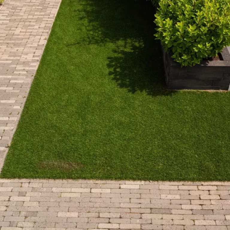 Kunstgras omrand door lichte waalformaat klinkers met plantenbak en struiken