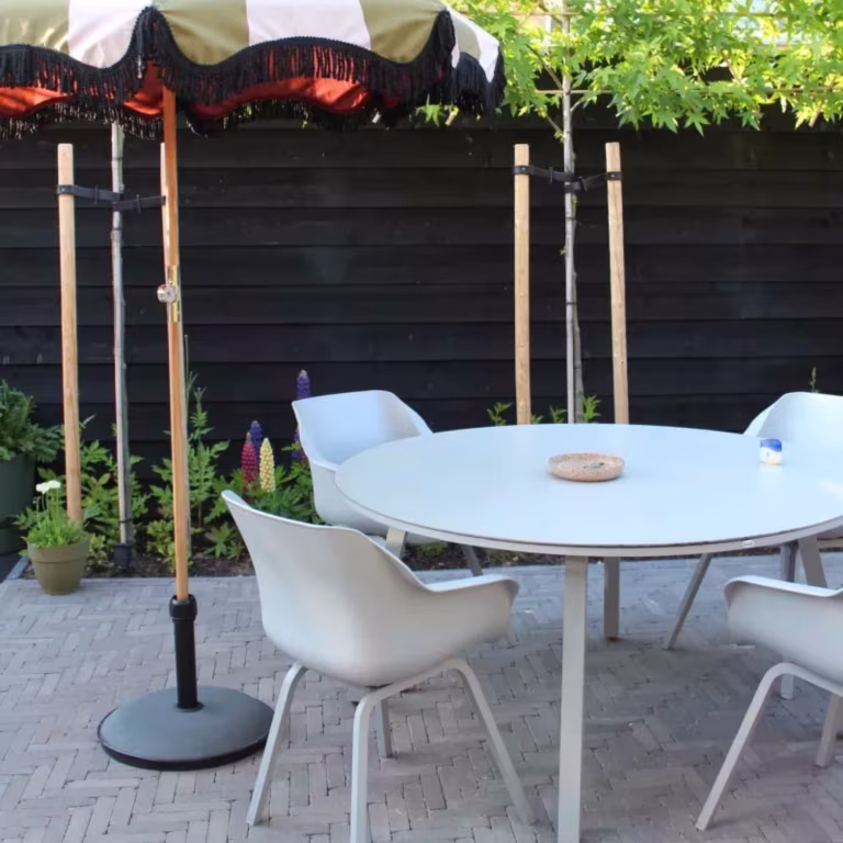 Ronde witte tuintafel met stoelen op Tambour Mangaan waalformaat voor zwarte schutting