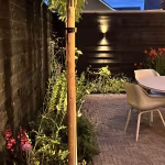 Avondverlichte tuin met zwarte schutting, wandlamp en Tambour Mangaan waalformaat in visgraat