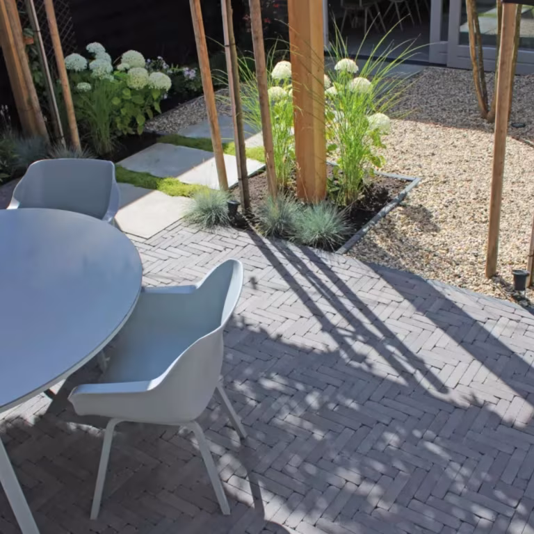 Terras met Tambour Mangaan in visgraat, grijze tuinstoelen, ronde tafel en houten palen