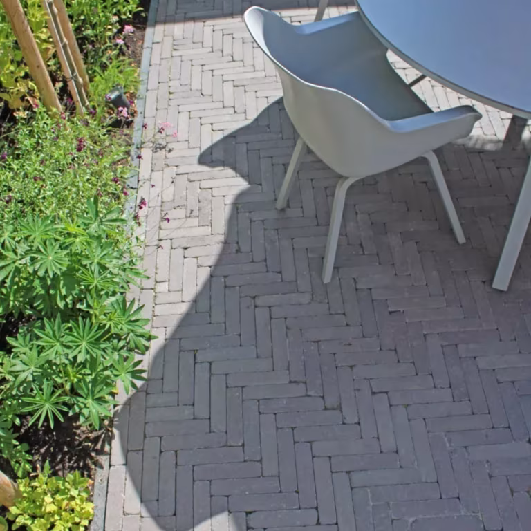 Tambour Mangaan waalformaat in visgraatverband met tuinstoel in schaduw naast border