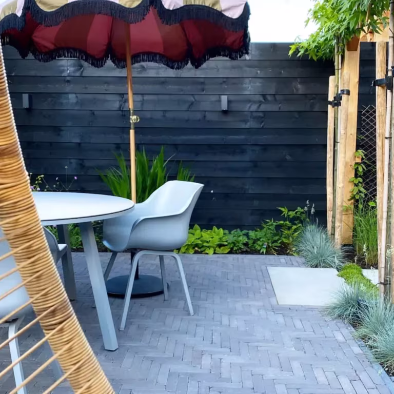 Tuinterras met Tambour Mangaan in visgraat, zwarte schutting, parasol en grijze tuinstoelen