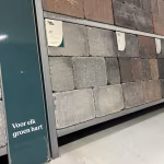 Showroomwand met Tuinvisie stenen in grijze en bruine tinten, schuin gezien met labels