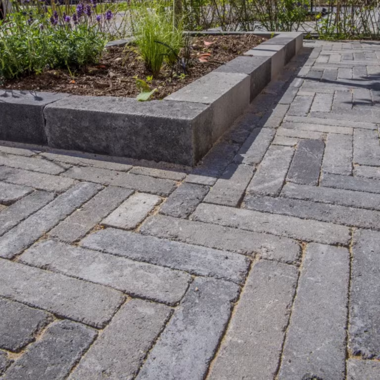 Verhoogde plantenbak van antracietkleurige blokken naast Tambour Smook klinkers in visgraatverband
