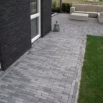 Pad van Tambour Smook klinkers langs zwarte gevel met loungebank op groot terras