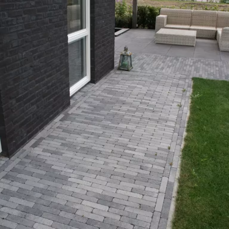Pad van Tambour Smook klinkers langs zwarte gevel met loungebank op groot terras