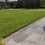 Tambour Smook stenenpad langs gazon met tuinmeubels en trampoline op achtergrond