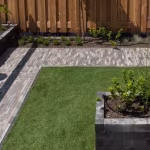 Tuin met Tambour Smook klinkerpad, kunstgras, houten schutting en plantenbak van antracietblokken