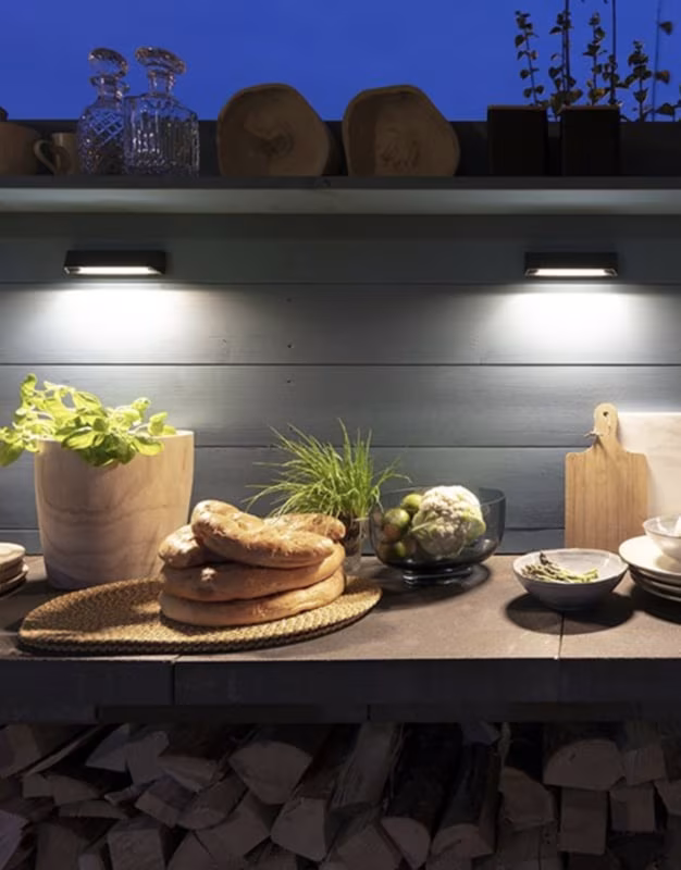 Wedge Slim wandlampen boven buitenkeuken met brood en houtopslag in de avond