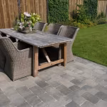 Terras van Tambour Smook bestrating met houten eettafel en rieten stoelen naast gazon