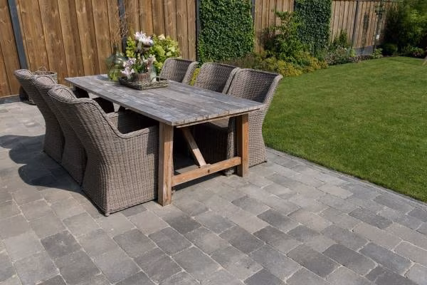 Terras van Tambour Smook bestrating met houten eettafel en rieten stoelen naast gazon