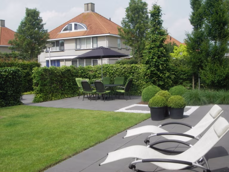 Terras met Soft Comfort Nero tegels, ligstoelen, buxusbollen en grasveld