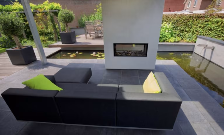 Loungebank met groene kussens naast vuurplaats en vijver op antraciet Schellevis tegels