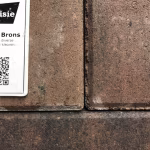 Showroomstaal Tremico Brons met label en QR-code naast klinkers in bruine tinten