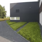 Gebogen pad met opsluitband langs siergrasborders naast zwart gebouw