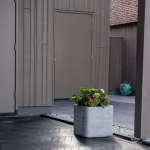 Zwarte visgraatbestrating Romano Punto Nero bij grijze berging met plantenbak en bloemen