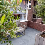 Binnentuin met Kera Full Body Leuven tegels, houten bank, olijftak en bakstenen muurtje