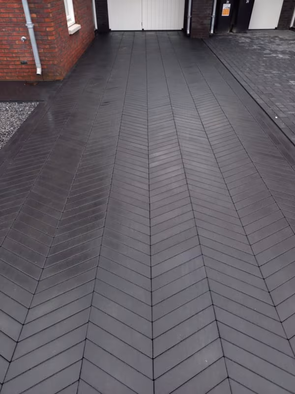Oprit met Romano Punto Nero visgraatbestrating in zwart naar garagedeuren