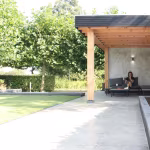 Terras met Kera Full Body tegels onder houten pergola, zittende vrouw en gazon