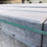 Close-up van gestapelde grijze Tremico betonklinkers met groene bandstrip op pallet