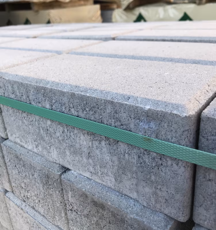 Close-up van gestapelde grijze Tremico betonklinkers met groene bandstrip op pallet