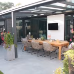 Terras onder glazen overkapping met lange eettafel en rotan stoelen op Kera Full Body Bastogne
