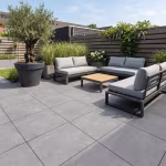 Terras met grijze tegels, loungehoek, olijfboom in grote pot en houten schutting