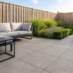 Tuin met Cilento Taupe terras, loungebank met kussens, border met siergras en houten schutting
