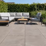 Terras met grijsbeige keramische tegels, loungehoek en tuinhaag op de achtergrond