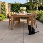 Houten eettafel met stoelen en zwarte kat op terras met grijsbeige keramische tegels