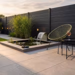 Terras met Kera Full Body Rome tegels, vijver met waterval, designstoel en zwarte schutting