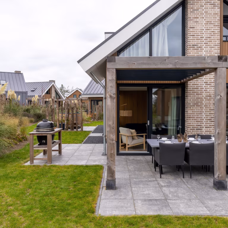 Houten pergola met eettafel op GeoCorso Pescara tegels naast gazon en woning