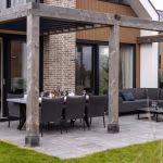 Pergola met zwarte tuinstoelen en eettafel op GeoCorso Pescara 60x60x4 tegels bij bakstenen pilaar