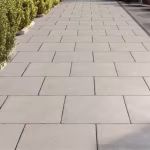 Grijze betontegels als stoep langs groene haag met smalle voegen