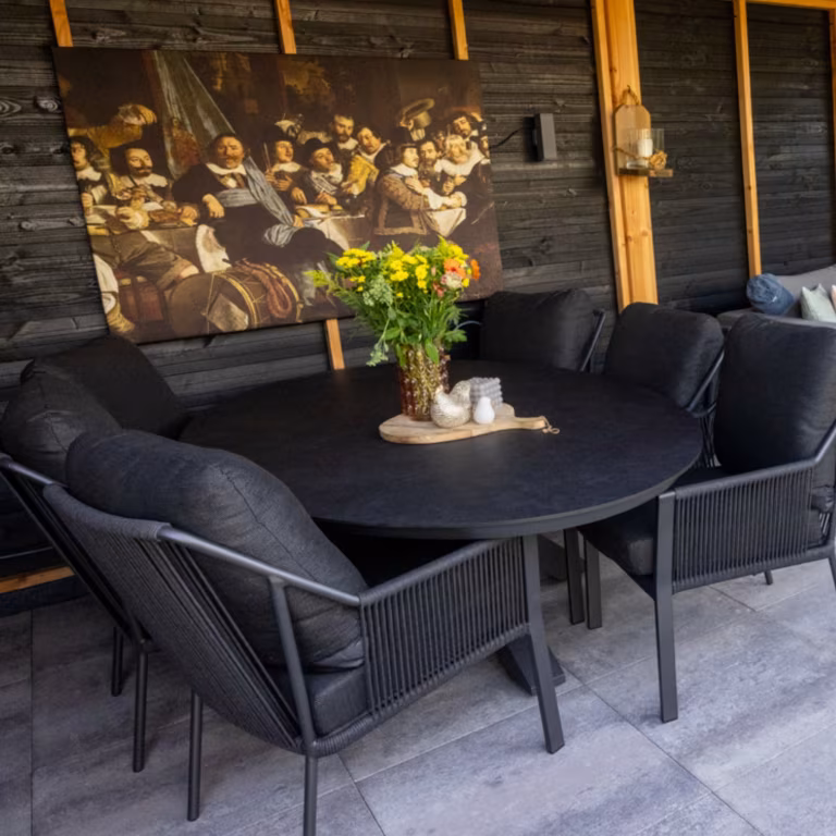 Zwarte eettafel met stoelen en bloemen op Soft Comfort Grezzo tegels onder overkapping