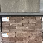 Showroomwand met gestapelde bruine WG Stone Trommelsteen 20x5x7 en artikellabels